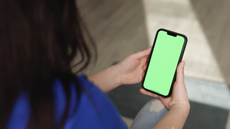 primer plano de una mujer sosteniendo un teléfono móvil inteligente y deslizando fotos o imágenes dejadas en el interior de un hogar acogedor. maqueta de llave de croma en el teléfono inteligente en la mano. use la pantalla verde para copiar el espacio