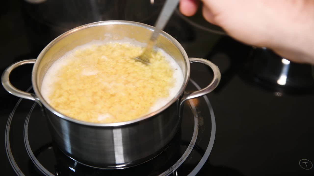 Preparazione di noodles per una zuppa tradizionale, primo piano, una mano maschile mescola il brodo denso e bollente.
