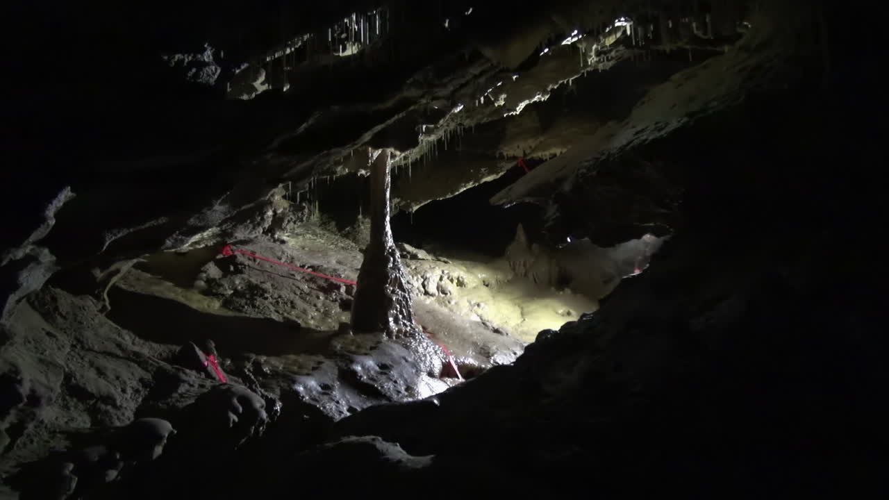 espeleólogo invisible ilumina la columna de calcita en la cámara de la cueva subterránea fangosa
