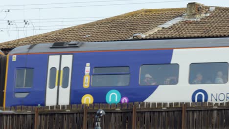 Modern passenger train moves past houses in daylight, side view, steady camera, urban environment