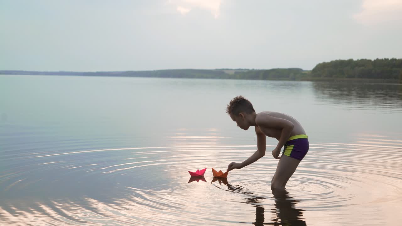 Little boy launch paper ship on the water. Beautiful summer sunset. Paper boat. Origami.