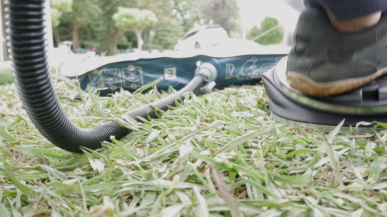 Foot presses pump to inflate air mattress on grass during outdoor setup