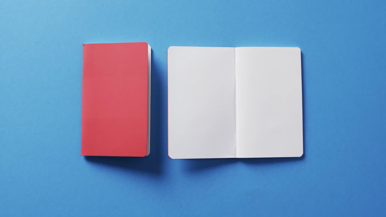 Close up of open blank book and red notebook with copy space on blue background in slow motion