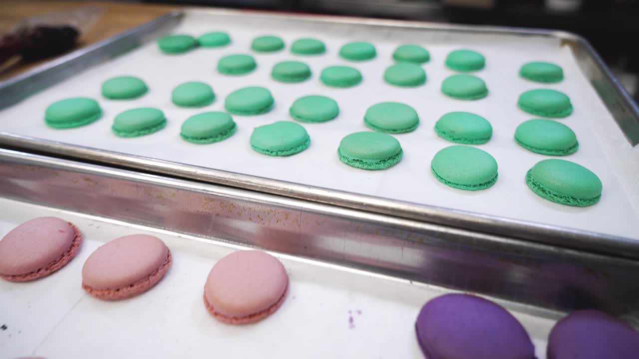 Dozens of freshly baked colorful macaron cookies, green pink purple french meringue cookie shells, close up 4K