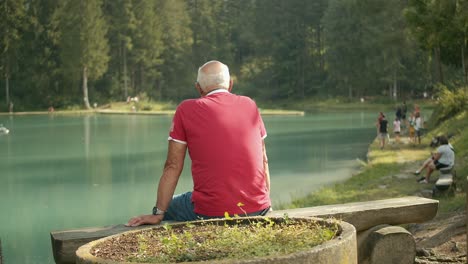 old man wearing red t-shirt relaxing in front of peaceful quiet lake