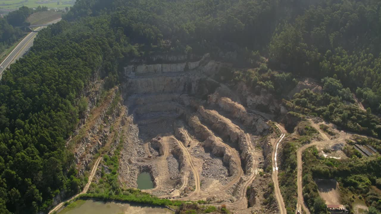 quarry in Barcelos, Portugal, with terraced rock formations and a nearby highway cutting through dense forest