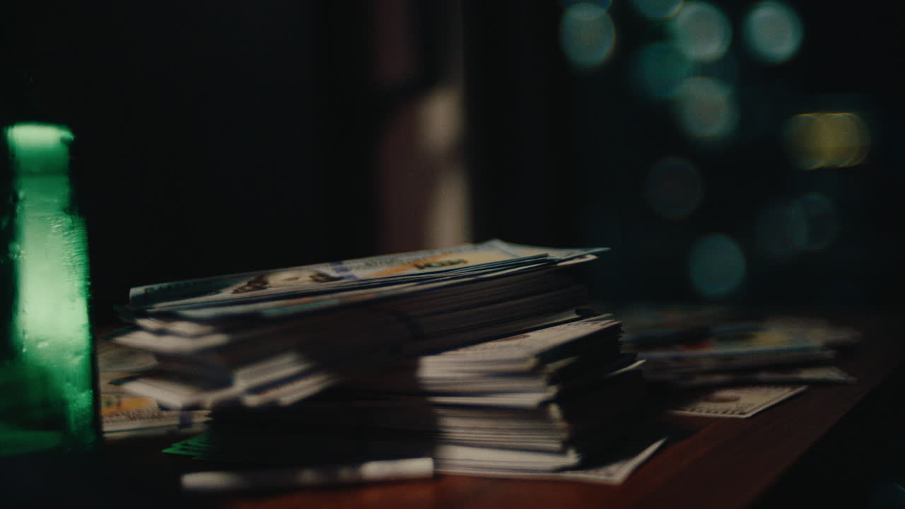 A cinematic close-up shot of stacks of US dollar bills neatly piled on a wooden desk, with soft urban bokeh lights and a green bottle in the background, symbolizing financial success