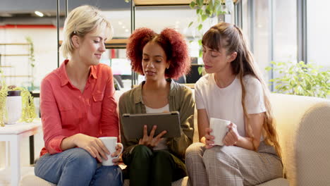 discussing creative writing ideas, three women holding coffee cups and using tablet