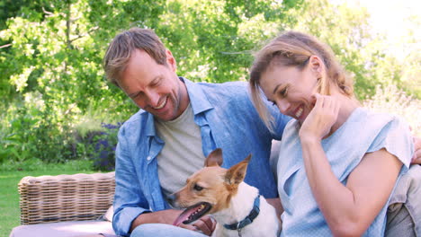 happy white couple sit petting their dog in the garden