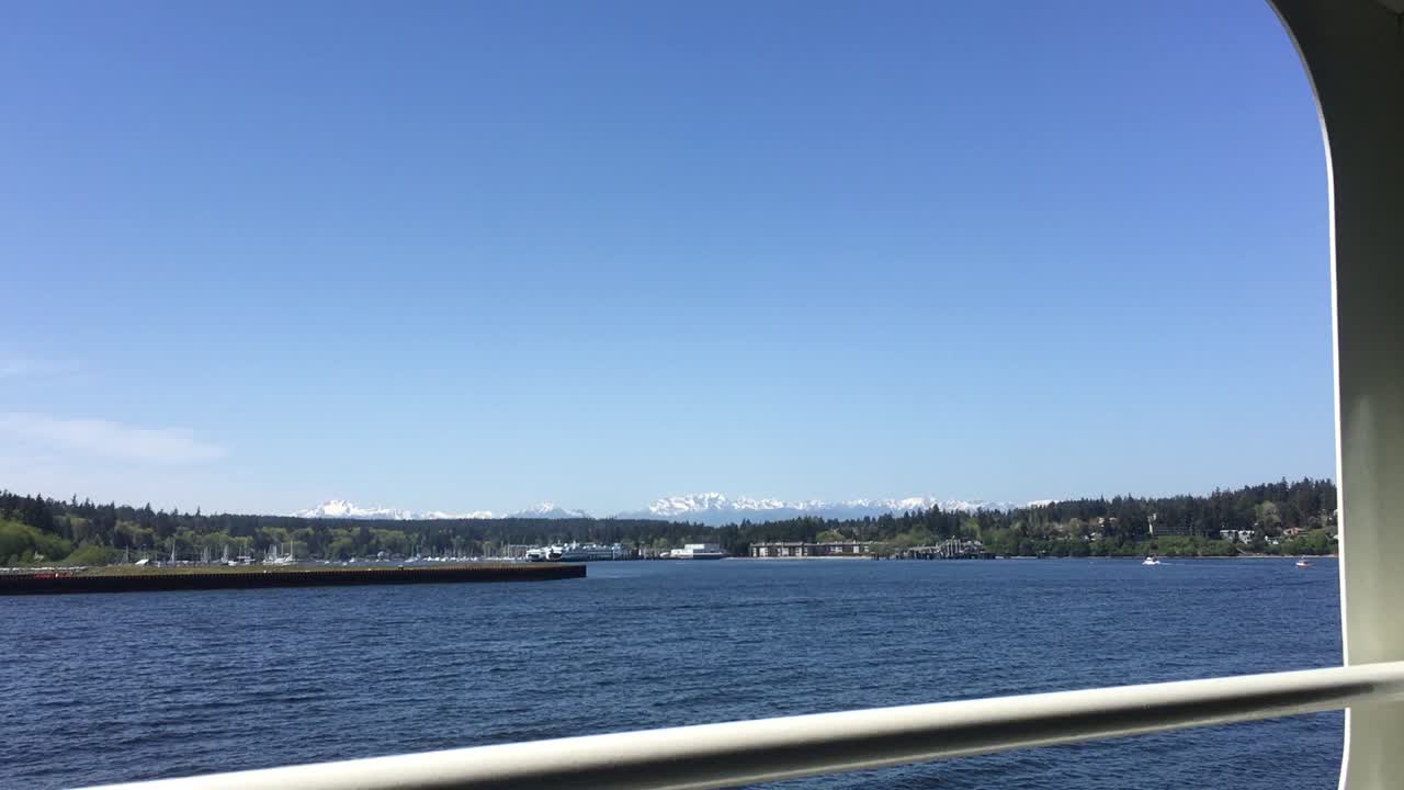 The Olympic Mountain Range behind small town of Winslow on Bainbridge Island Washington being approached by ferry boat