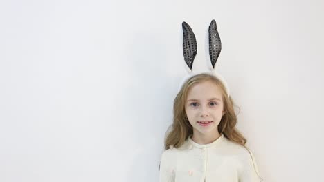 smiling little girl in a cloak, dressed in the ears of an easter bunny, a happy child is waiting for the holidays, on a white background