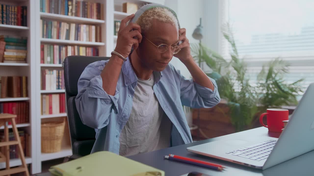 Handsome darkskinned man listening to music on headphones and typing on laptop