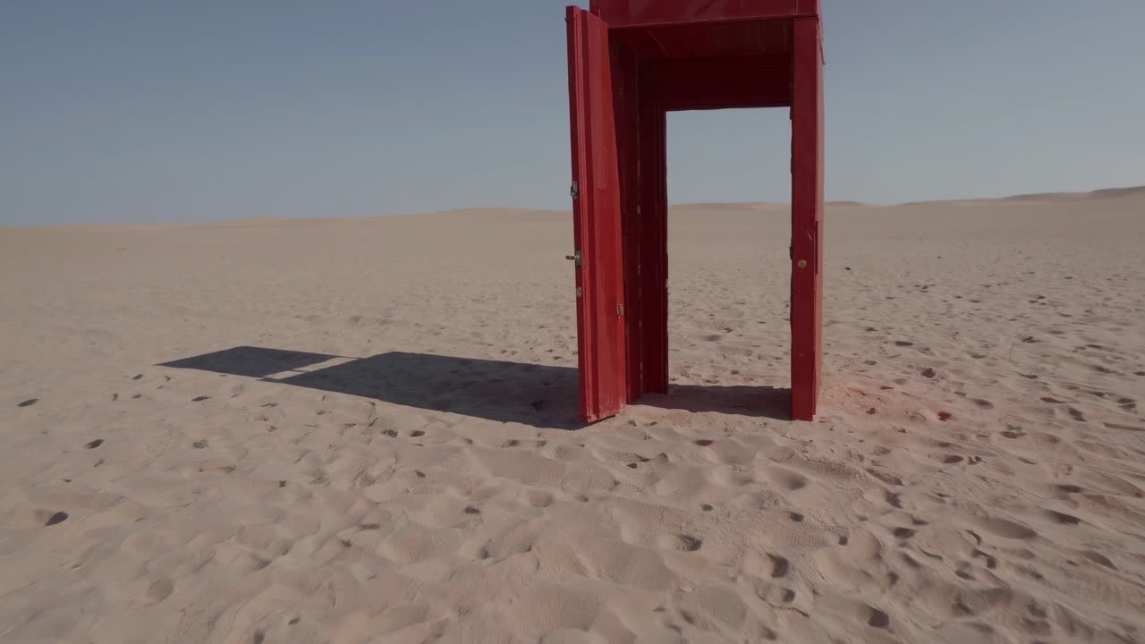 Aged crimson wooden portal standing alone amid arid terrain, slowly swinging open, revealing desolate wilderness representing personal transformation and hidden possibilities
