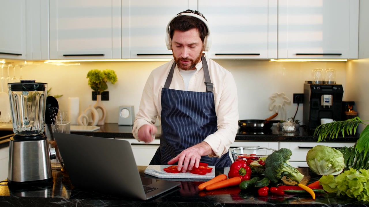 Midaldrende mand med hovedtelefoner laver sund salat til live stream madlavnings-vlog i hjemmekøkken