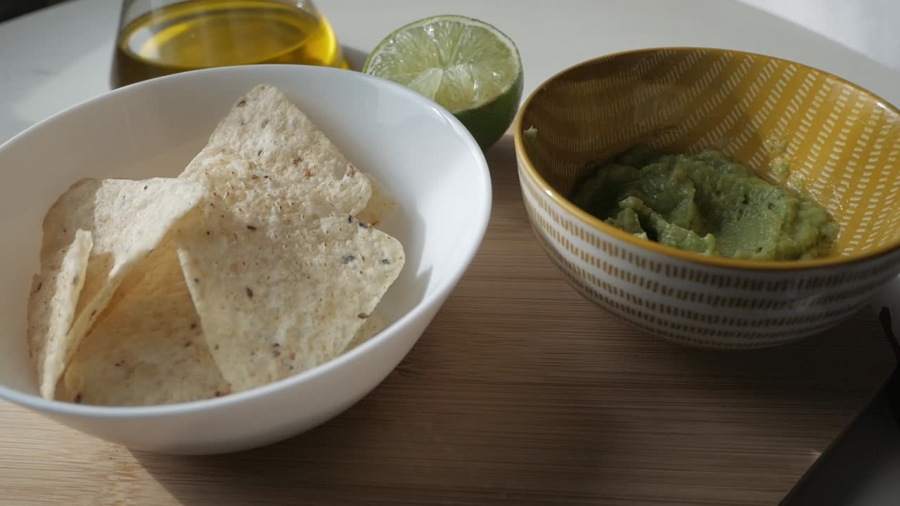 Fresh guacamole served with tortilla chips, lime wedge, and olive oil in the background