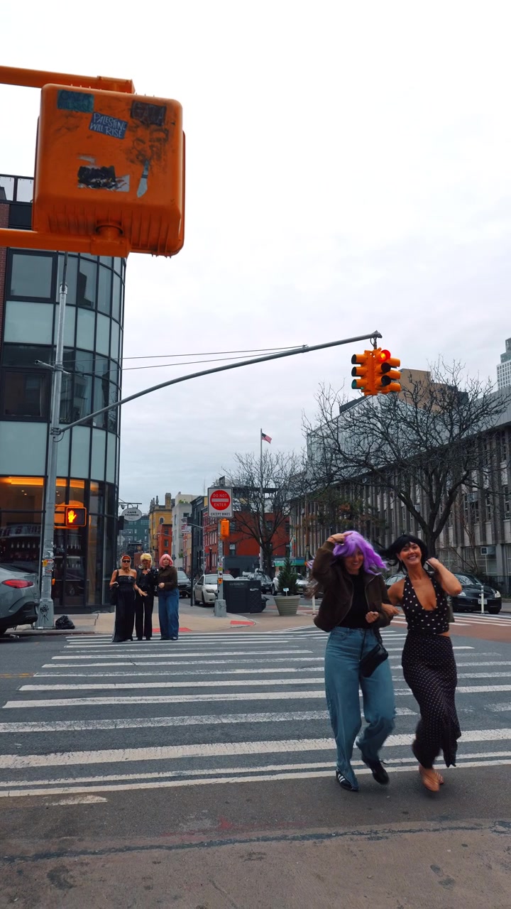 New York, USA, 1 May 2026: People in Colorful Wigs Crossing NYC Street Halloween. Women in colorful wigs crossing urban intersection, red traffic light, orange pedestrian signal box
