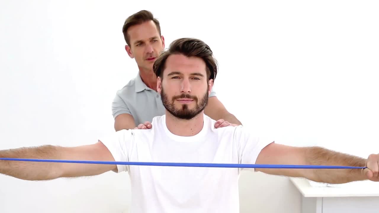 Fisioterapista che controlla le spalle del paziente con una fascia elastica di resistenza