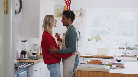 Loving-Couple-Wearing-Fancy-Dress-Antlers-Dancing-In-Kitchen-Whilst-Preparing-Christmas-Dinner