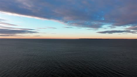 una vista aérea sobre el océano volando hacia el horizonte durante el amanecer en una mañana nublada