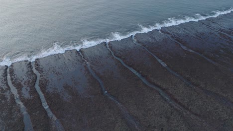 Stationary-Drone-shot-of-Bingin-Beach-low-tide-reef-and-waves-at-sunset-in-Uluwatu-Bali-Indonesia