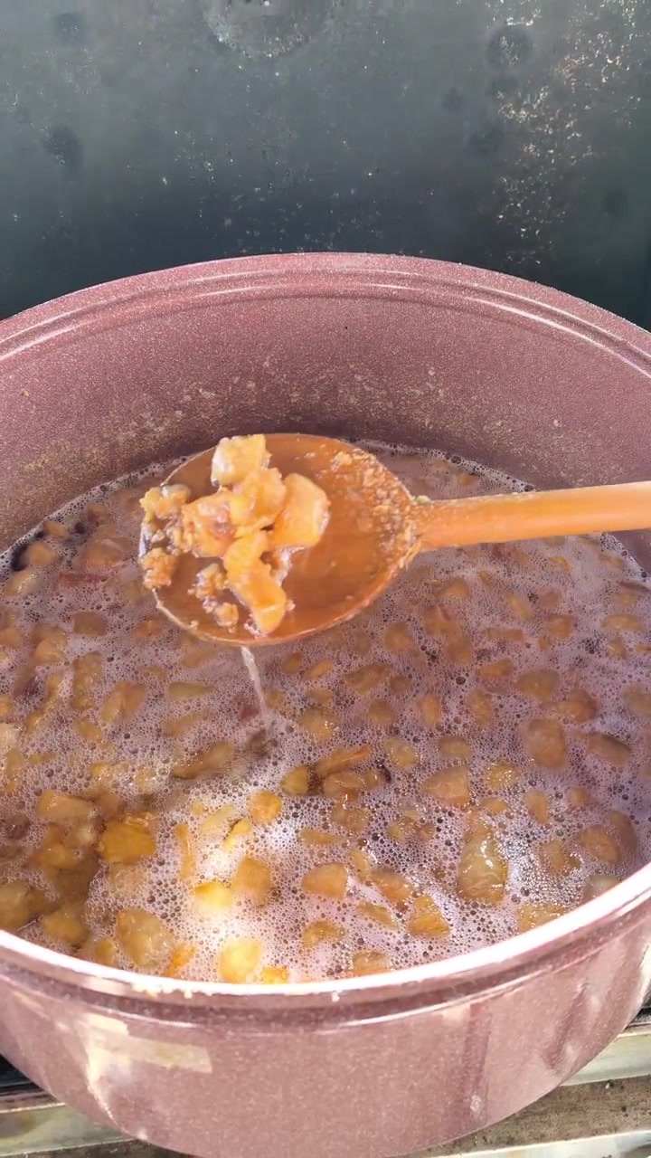 Scatto verticale della cottura e mescolatura di ciccioli in una grande pentola durante la preparazione tradizionale di cibo all'aperto.