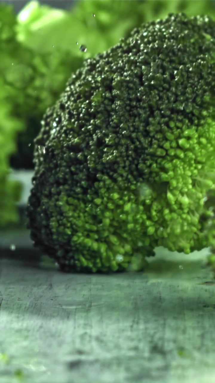 Cimette di broccoli freschi e verdi che cadono con gocce d'acqua al rallentatore.
