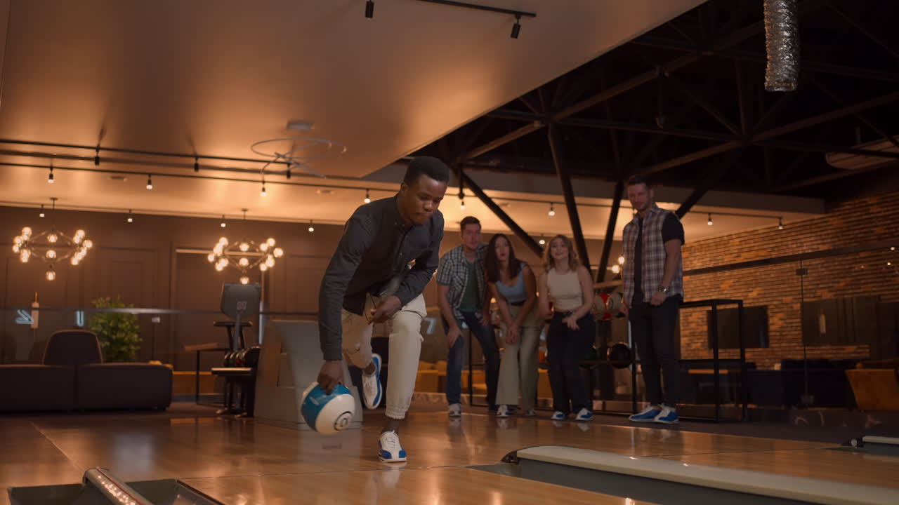 An African-American throws a bowling ball and knocks out a shot with one shot. Multi-ethnic group of friends bowling