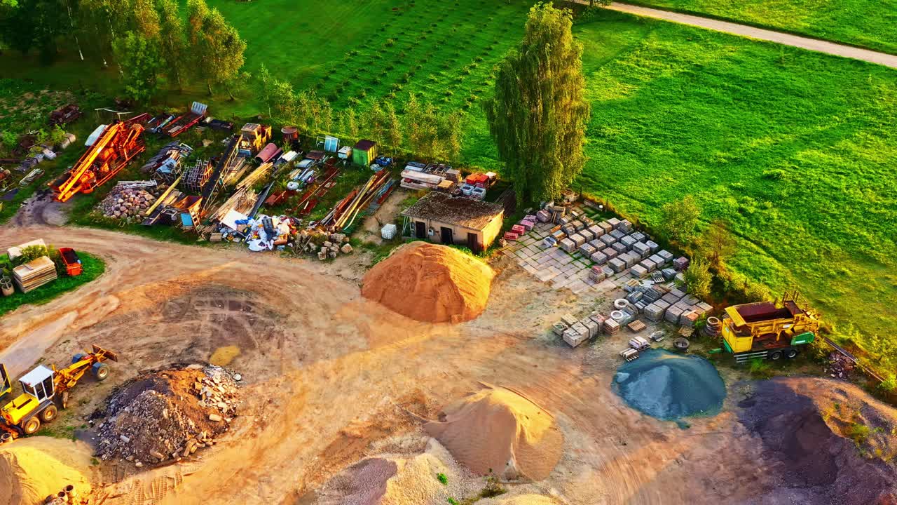 Gravel and material depot with various construction supplies and vehicles in storage yard