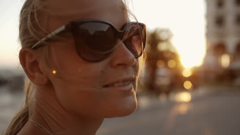 mujer sonriente con gafas de sol al aire libre durante la puesta de sol