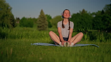 already settled on her yoga mat, a young woman draws energy from the warm evening sun. the camera gently pulls back and travels left, revealing the peaceful beauty of nature around her.