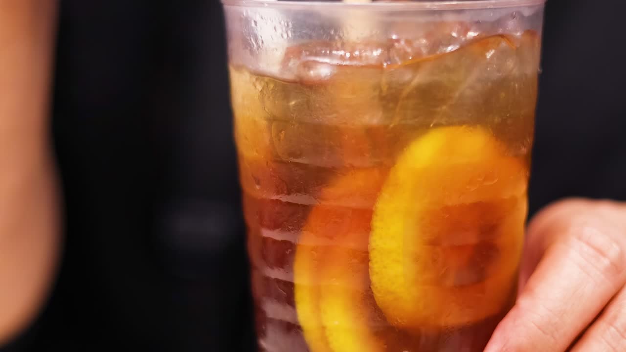 A hand holds a glass of iced tea with lemon slices, showcasing refreshing details.