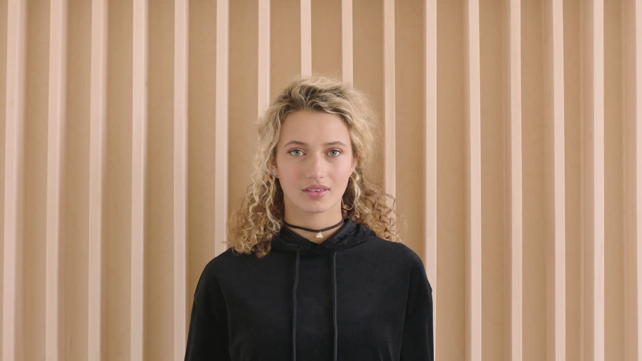 retrato en cámara lenta de una joven rubia linda que parece pensativa, tímida ante la cámara, vulnerable, femenina con capucha negra