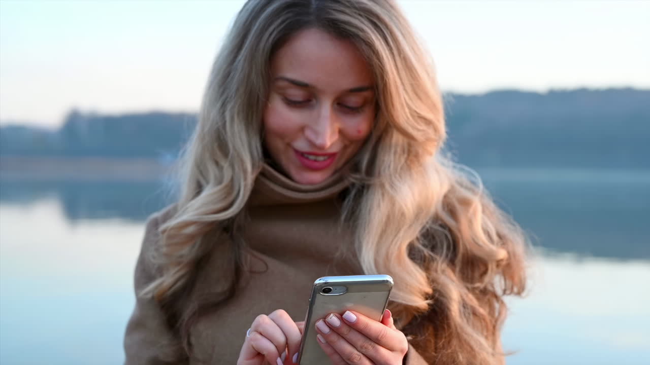 Smilende ung kvinde, der taster på sin telefon i parken