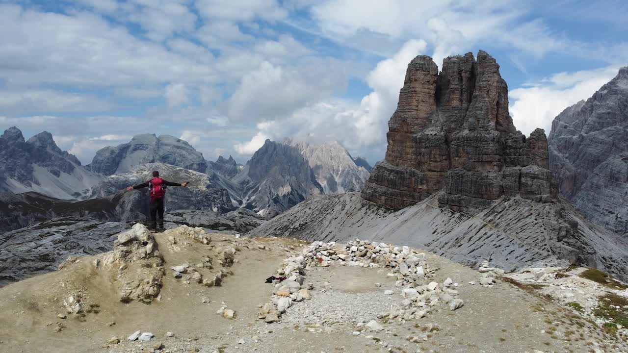 En vandrer står alene i bjergene og fejrer en eventyrlig og succesfuld vandretur i Dolomitterne i Italien - Sydtyrol