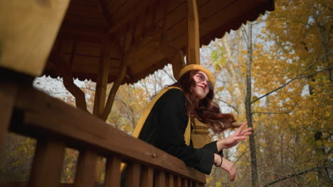 dama feliz tocando su cabello lúdicamente mientras descansa su mano en la cuña del mirador, rodeada por un telón de fondo vibrante de árboles de otoño
