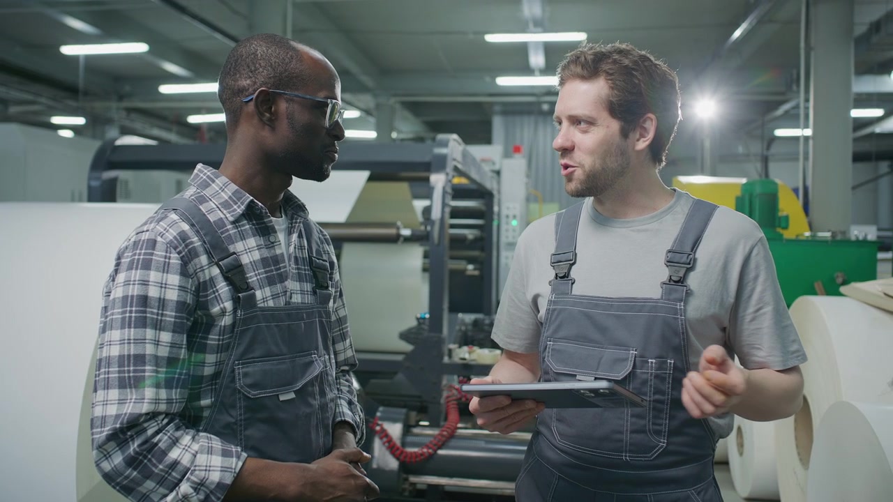 Printing Plant Technician Speaking with Quality Control Inspector Using Tablet