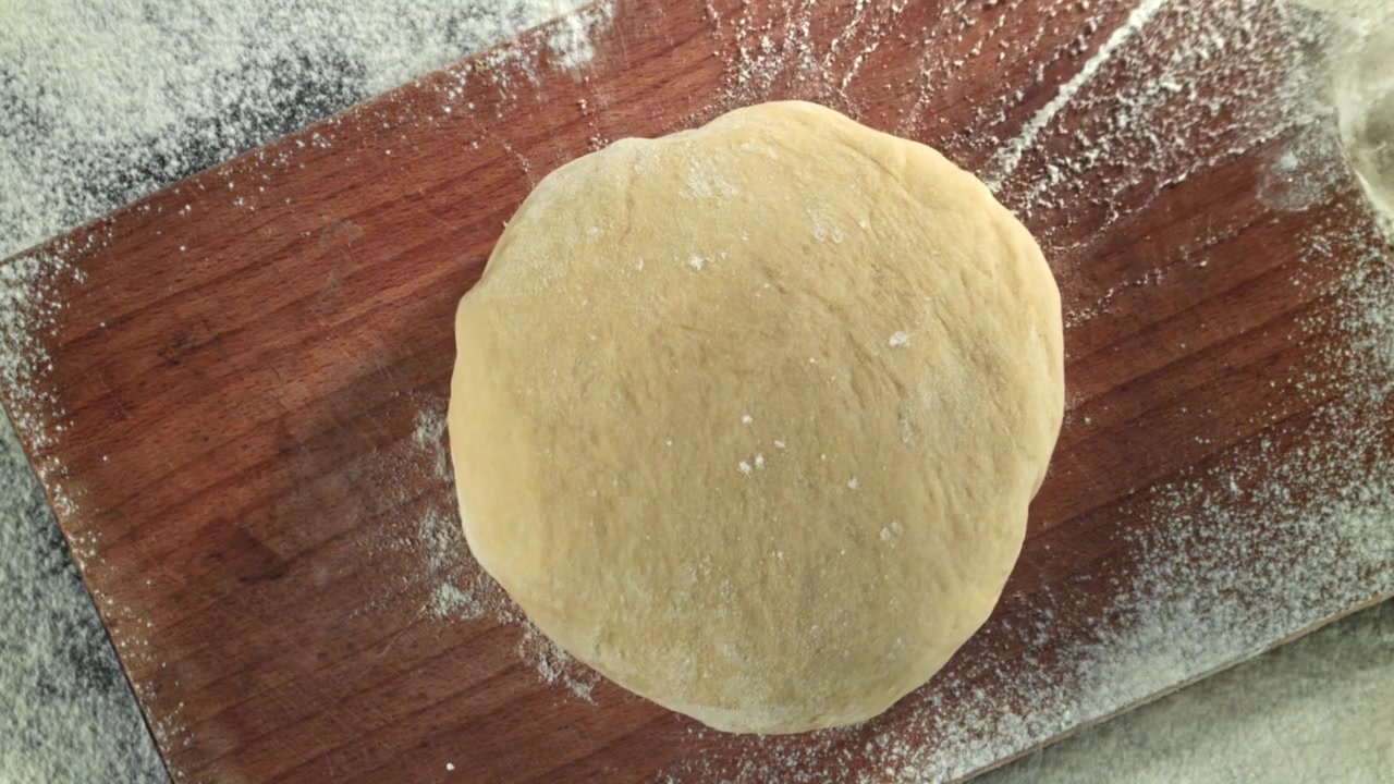 Farina spolverata su impasto crudo su un tagliere di legno