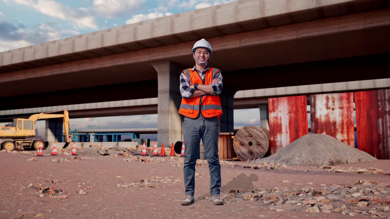 Full Body Of Asian Male Engineer With Safety Helmet Crossing His Arms And Smiling To Camera While Standing At The Site of Highway Construction