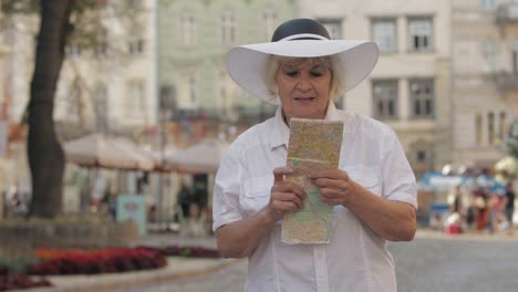 senior female tourist exploring town with a map in hands. looking for the route