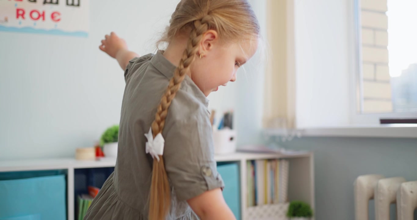 Little Girl Looking at Books on a Shelf in Classroom