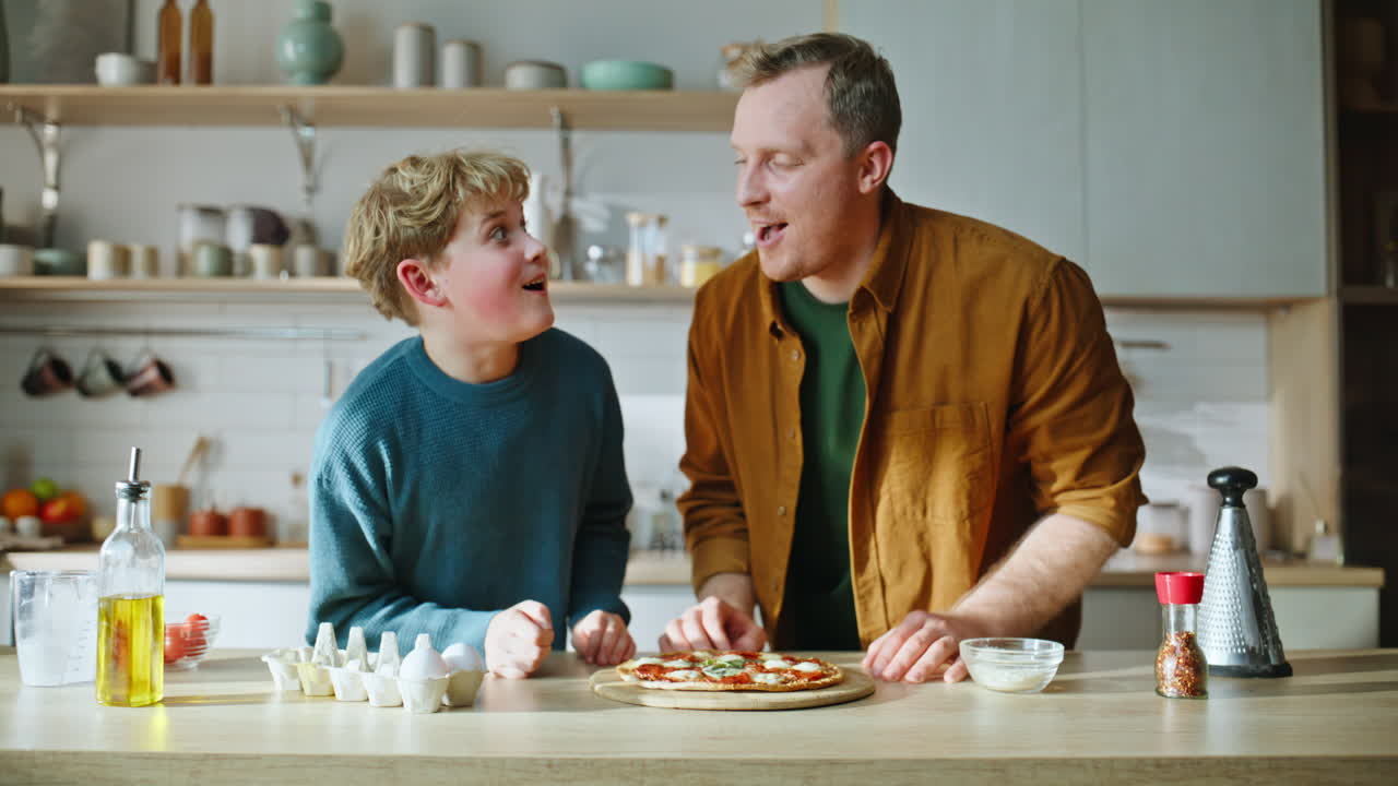 Vater und Sohn schnuppern an Pizza, genießen gemeinsam hausgemachtes Essen, stehen in der Küche, Nahaufnahme