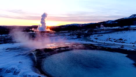 panoramic view of a geyser in geysir, iceland. a lot of smoke is getting out of the geyser with people walking all around the geyser, under the red sunset.