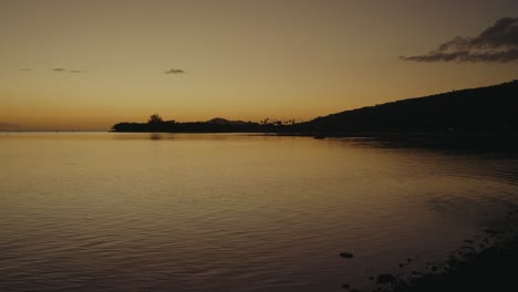 las montañas volcánicas de oahu (hawaii) son una silueta contra el cielo naranja mientras se refleja en las aguas tranquilas del océano pacífico justo después de la puesta de sol.