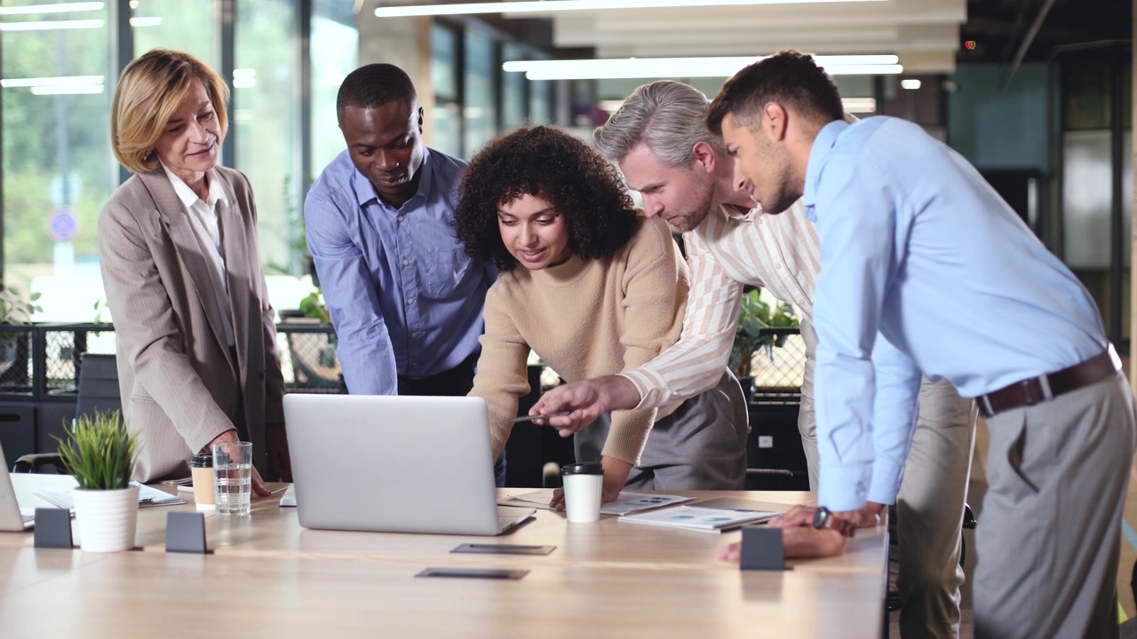 Equipa de negócios diversificada colaborando em laptop em escritório moderno
