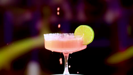 a pink margarita is poured into a glass with a lime garnish, set against a colorful, blurred background