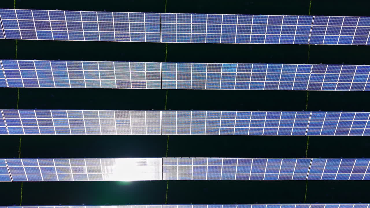 Pannelli solari disposti in file coprono una vasta area in una giornata di sole in un campo di energia rinnovabile vicino a una località rurale.