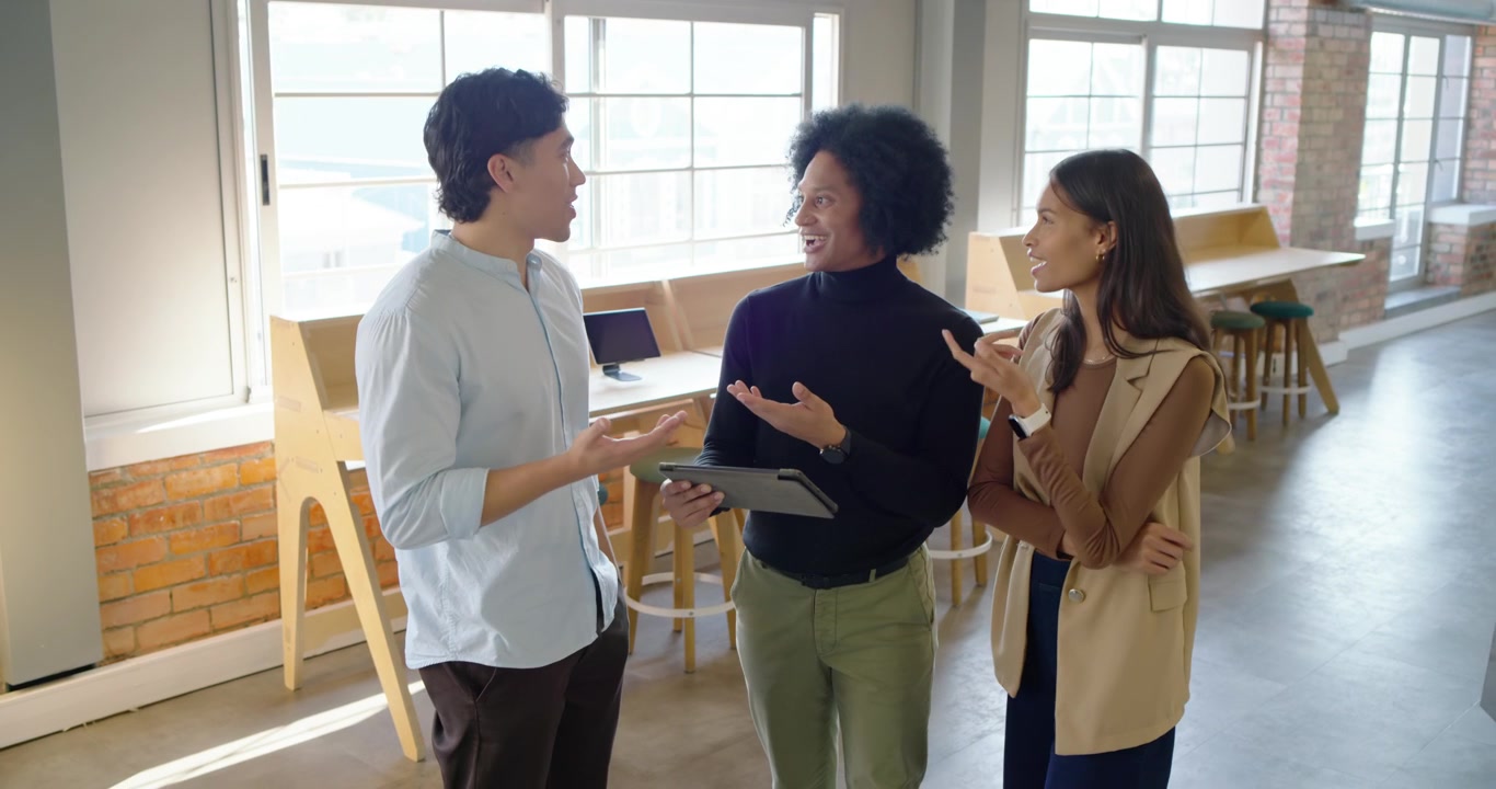 明るいオフィスで多様な同僚たちが集まる中、中央のプレゼンターがタブレットのデモを始め、議論を導いている。