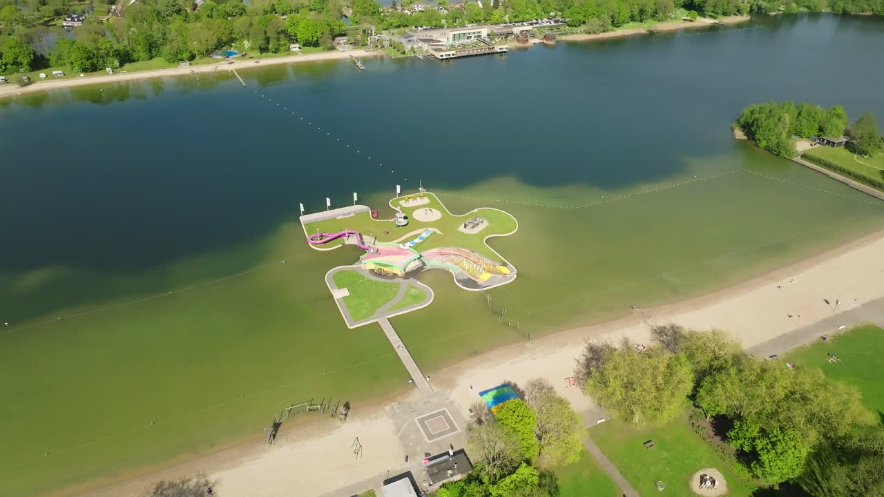 Colorful water playground on lake surrounded by sandy beach and green park during sunny summer day for families and children