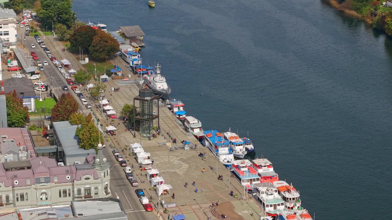 Cirkulär flygvy över Valdivias strandpromenad, Chile, och Foucaults pendel; ett experiment i Valdivia en solig dag; turistbåtar längs Calle Calle-flodens stränder.