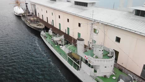 Aerial-view-of-two-Swedish-military-ships-docked-next-to-a-museum-in-Karlskrona,-Sweden